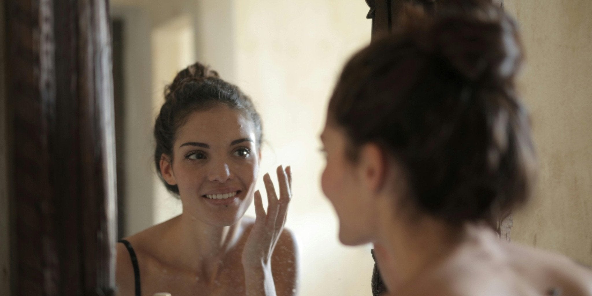 Žena ispred ogledala sa osmehom i zdravom kožom, rezultat redovnog ispijanja Premier Collagen