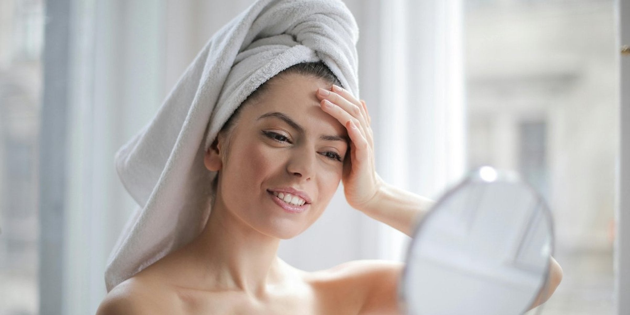 Žena sa peškirom na glavi gleda u ogledalo nakon tuširanja, blistava koža zahvaljujući konzumaciji Premier Collagen-a